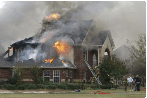 Single family home that is on fire with firefighters in the yard attempting to extinguish the flames.